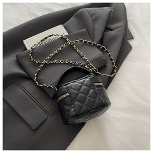 Detail of black quilted mini box bag with gold chain strap on grey blazer