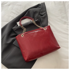 Close-up of red glossy leather tote bag with gold chain strap on grey blazer