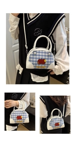 Detailed view of blue and white plaid handbag featuring red apple print and white straps