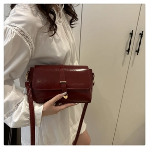 Détail d'un sac en cuir verni bordeaux avec boucle en métal doré en forme de cœur et sangle