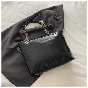 Detail of glossy black patent leather tote with gold chain strap on grey blazer