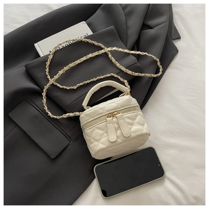 Detail of white quilted mini box bag with gold chain strap and dual zipper on a blazer
