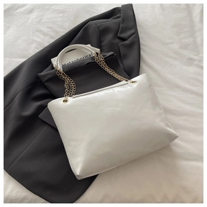Detail of white tote bag with gold chain strap on a dark grey blazer background