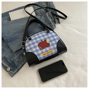 Detail of blue plaid handbag with red apple graphic and black leather accents