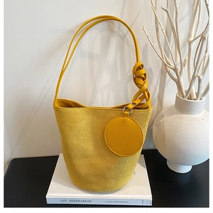 Détail du sac seau en daim jaune avec bandoulière nouée et pendentif circulaire