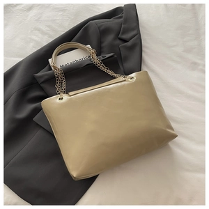 Detailed top view of a large beige tote bag with gold chain handles on a blazer