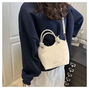 Modèle portant un sac seau crème texturé avec lettrage doré et détails de bandoulière