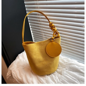 Détail du sac seau en daim jaune avec nœuds tressés et breloque décorative en cuir