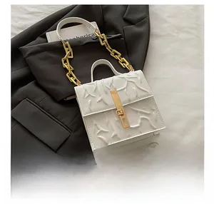 Detailed view of the white embossed texture and chunky gold chain handle on the bag
