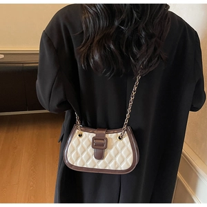 Dettaglio borsa trapuntata crema con bordo marrone e catena dorata su cappotto nero