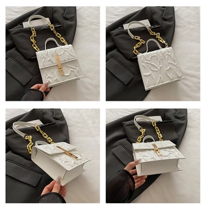 Detail view of white pleated handbag with gold chain strap and square metal lock closure