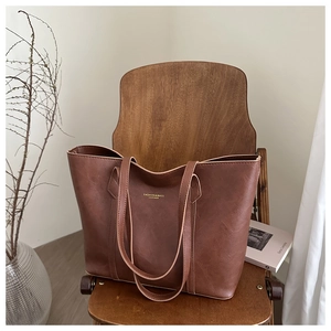 Gros plan d'un cabas en cuir marron avec lettrage doré sur un fond de chaise en bois