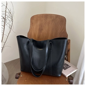 Détail du sac cabas en cuir noir avec logo doré posé sur une chaise en bois élégante