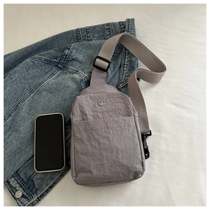 Close-up of gray nylon chest bag featuring a metal M logo and adjustable woven strap