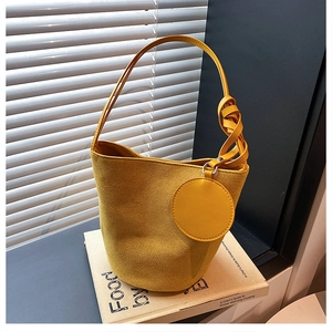 Détail du sac seau en daim jaune avec poignée tressée posé sur un livre ancien