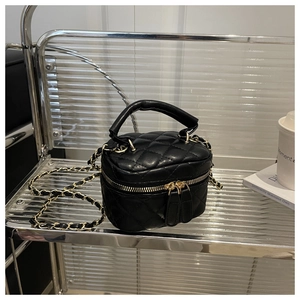 Detail of black quilted mini vanity bag with leather handle and metal chain strap