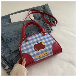 Close-up of blue gingham crossbody bag with apple pattern and red leather handles