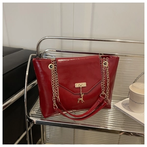 Detail of red high-gloss tote with gold chain strap and elegant deer charm on glass shelf