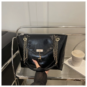 Detail of black patent leather tote bag with gold chain and metal deer charm