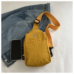 Detail of yellow nylon chest bag with metallic M logo and adjustable strap next to a phone
