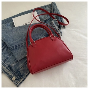 Close-up of red leather shell bag with adjustable strap on denim jacket background