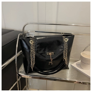 Detail of black glossy handbag with golden chain strap and deer pendant on a shelf