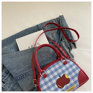 Close-up of blue and white checkered handbag featuring a red apple graphic and top handle