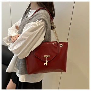 Detail of red glossy tote bag with golden deer charm and chain shoulder strap on model
