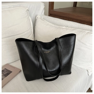 Grand sac cabas noir en similicuir avec lettrage doré posé sur un canapé blanc élégant