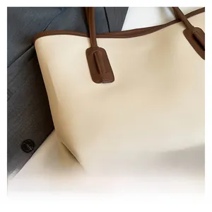 Detail of cream tote bag featuring brown contrast trim and precision stitching on handles