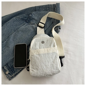 Detail of white nylon chest bag with adjustable strap next to a phone for scale