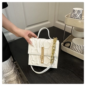 Detailed view of white embossed leather handbag with gold chain and rectangular metal lock