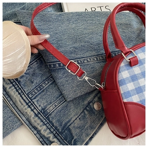 Detail of red leather crossbody bag with blue plaid fabric and silver metal hardware