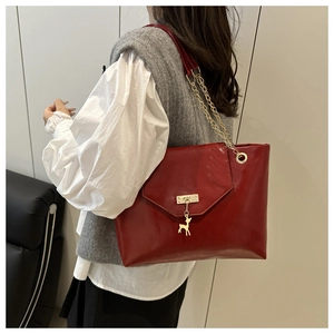 Detail of red leather tote bag showing golden chain strap and deer pendant on model