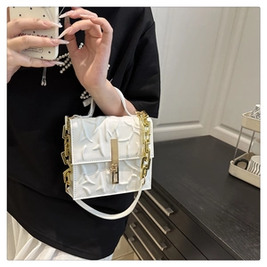 Close-up of white embossed leather bag with thick gold chain and metallic buckle detail