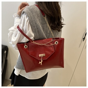 Detail of red glossy shoulder bag with gold deer pendant and chain strap on model