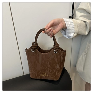 Détail du sac seau marron foncé avec texture plissée et logo doré sur le devant