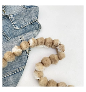 Detailed close-up of fuzzy brown and white plush pom-pom shoulder strap on denim