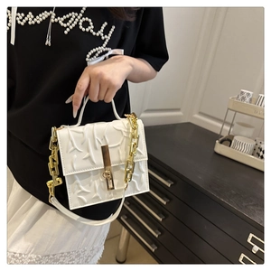 Close-up of white crossbody bag with textured embossing and golden chain strap detail