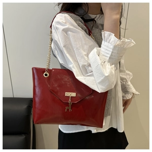 Detail of red patent leather tote bag featuring a gold chain strap and deer charm accessory
