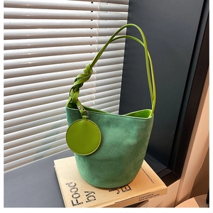 Sac seau en daim vert avec poignée nouée et breloque ronde posé sur un rebord de fenêtre