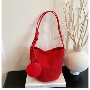 Détail du sac seau rouge en suède avec bandoulière nouée et pochette ronde sur livre
