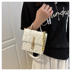 Close-up of white textured crossbody bag with thick gold chain and embossed pattern