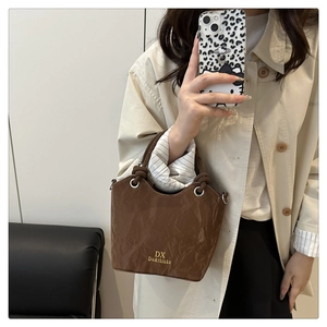 Détail du sac seau marron foncé avec texture plissée et lettrage doré de la marque