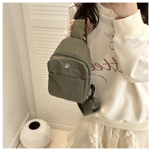 Detail der dunkelgrünen Nylon-Brusttasche mit M-Logo aus Metall und verstellbarem Gurt