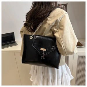 Close-up of black glossy leather tote bag with gold chain strap and deer pendant on a model