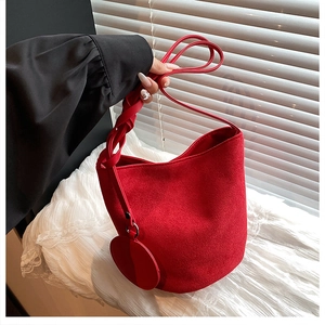 Gros plan du sac seau en velours rouge avec sangle tressée et breloque ronde