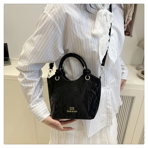 Détail du sac à main en cuir verni noir brillant avec logo doré et finitions argentées