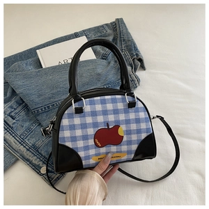 Detail of blue plaid shell bag with red apple pattern and black leather handle straps
