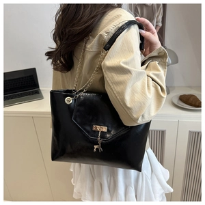 Detail of glossy black patent leather tote bag with gold chain strap and deer pendant